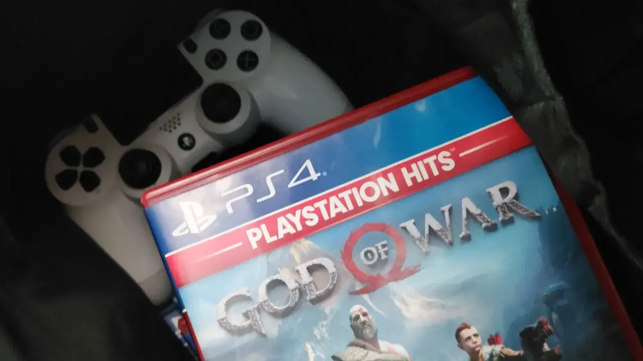 Dos mandos de PS4 y la carátula del juego "God of War", uno de los juegos exclusivos de PS4 más aclamados.