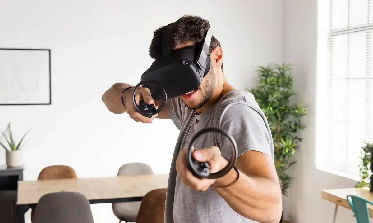 Hombre con casco de RV, inmerso en uno de los mejores juegos VR, con mandos en mano.