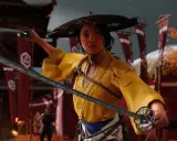 Una guerrera con un sombrero cónico y un kimono amarillo empuña dos katanas, lista para la batalla. Su mirada decidida es un reflejo de la guía que ofrece el **guia ghost of yotei**.
