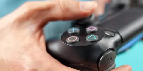Manos sujetando un mando de PS4, con enfoque en los botones.