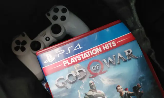 Dos mandos de PS4 y la carátula del juego "God of War", uno de los juegos exclusivos de PS4 más aclamados.