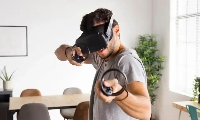 Hombre con casco de RV, inmerso en uno de los mejores juegos VR, con mandos en mano.