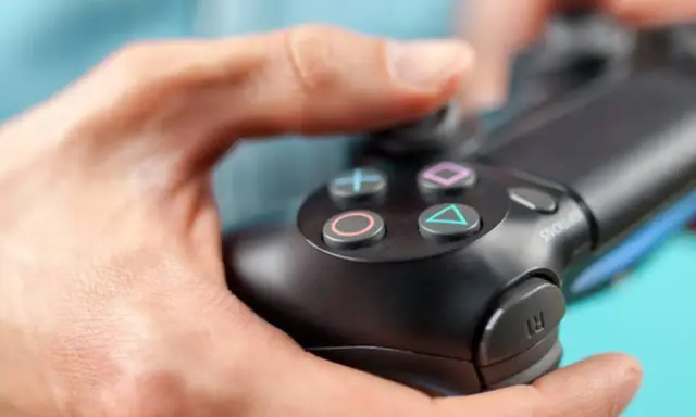 Manos sujetando un mando de PS4, con enfoque en los botones.