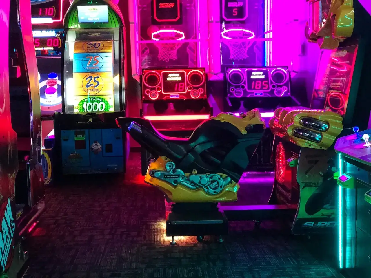 Máquinas de videojuegos de neón, incluyendo una de carreras de motos, listas para ofrecer los mejores juegos arcade.