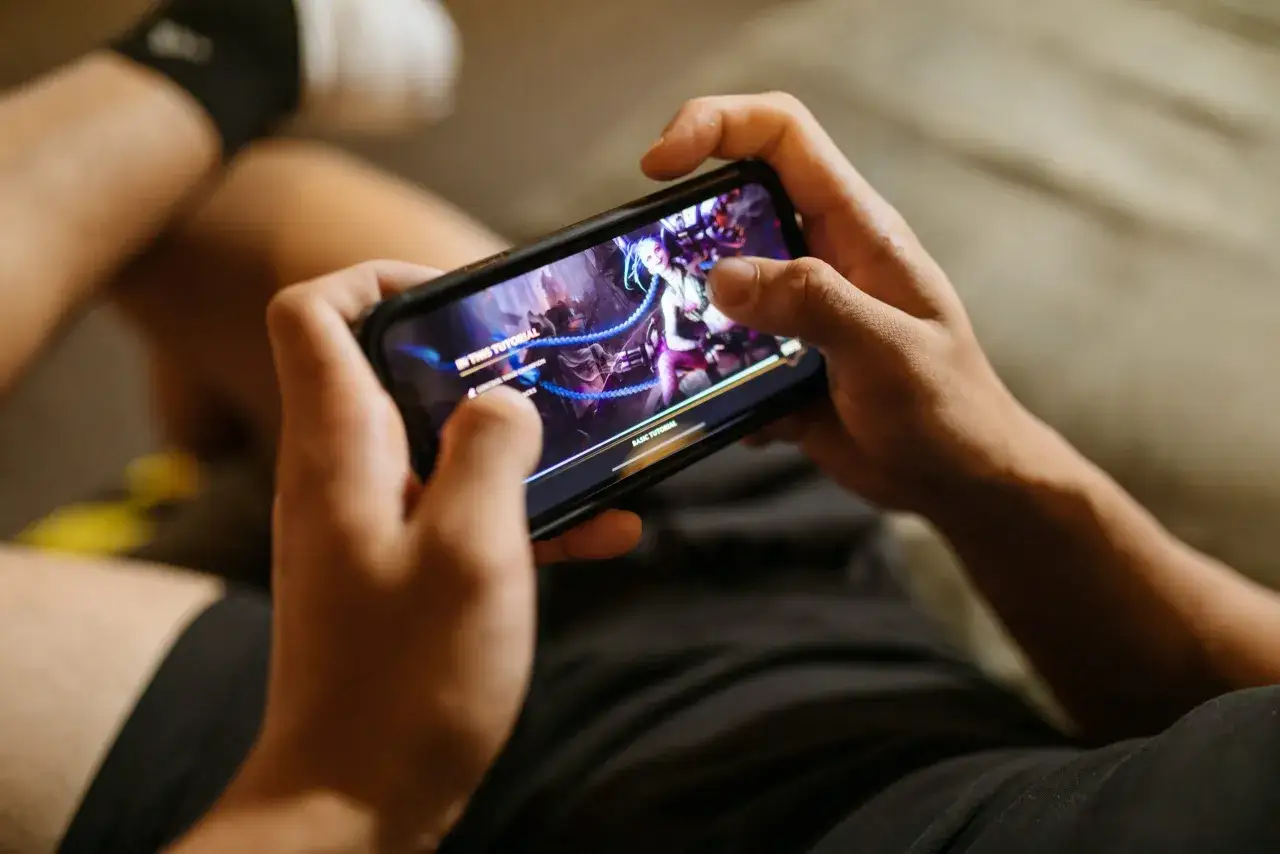 Persona jugando juegos para iPhone, con un personaje femenino de cabello azul en la pantalla.